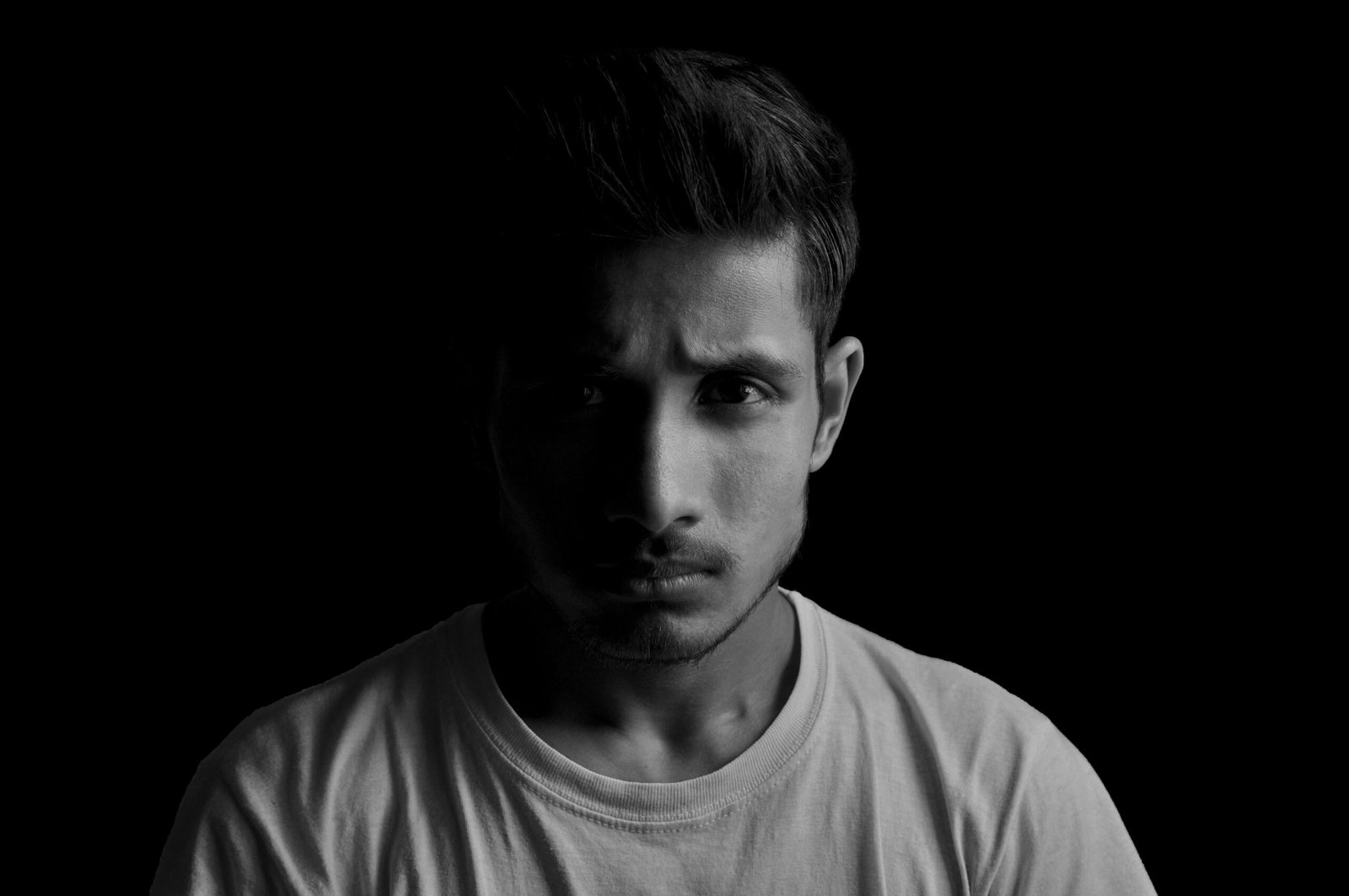 Dramatic black and white portrait of a young man with serious expression and dark background.